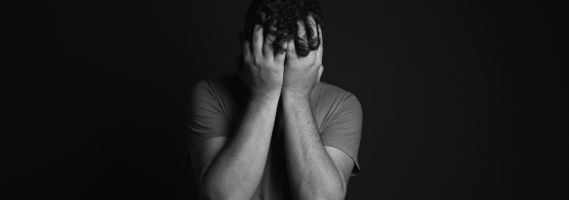 Picture is a black and white image featuring a man with his head in his hands.